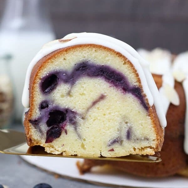 A slice of blueberry almond bundt cake lifted up on a gold cake server.