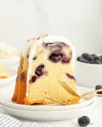 A slice of blueberry almond bundt cake topped with cream cheese icing on a plate.