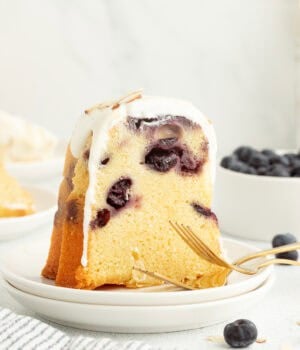 A slice of blueberry almond bundt cake topped with cream cheese icing on a plate.