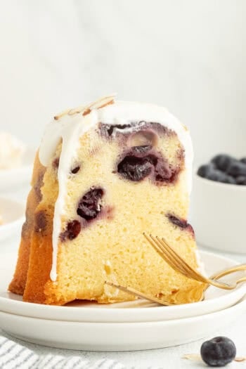 A slice of blueberry almond bundt cake topped with cream cheese icing on a plate.
