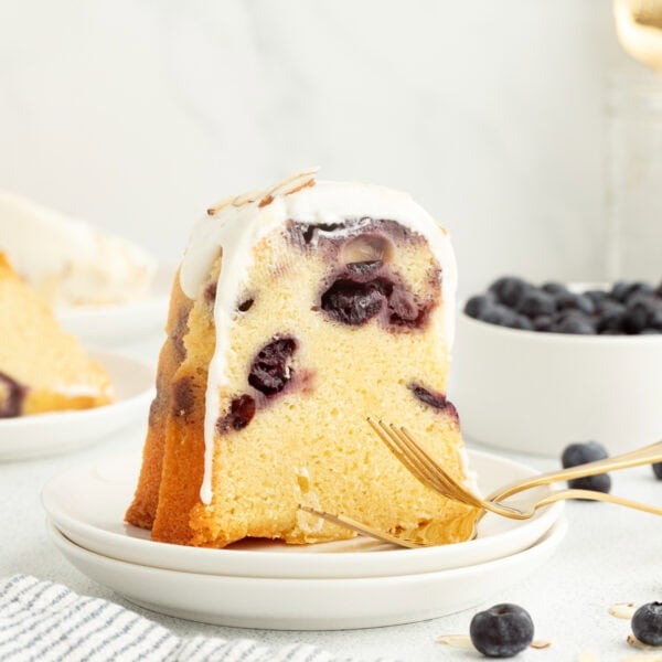 A slice of blueberry almond bundt cake topped with cream cheese icing on a plate.