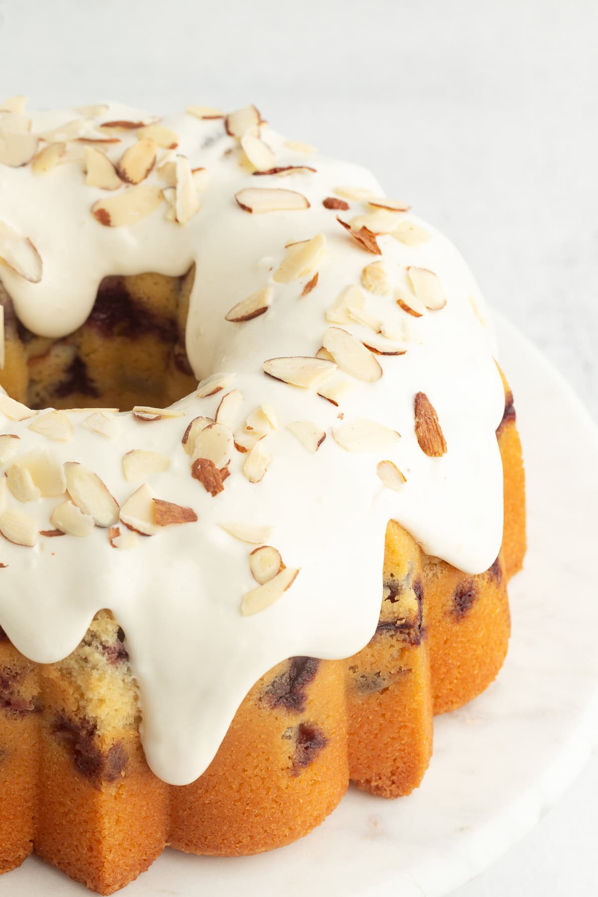 This blueberry bundt cake is a moist pound cake recipe with added almond flavor and juicy blueberries, topped with tangy cream cheese icing. Blueberry bundt cake topped with cream cheese icing and slivered almonds.