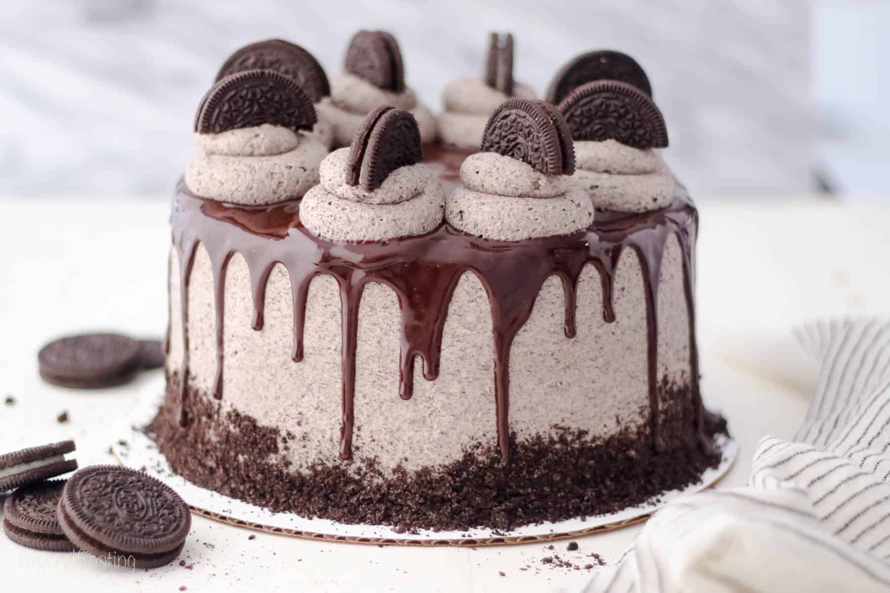 An Oreo cookies and cream cake on a cake plate decorated with a chocolate drizzle, swirls of Oreo frosting, and Oreo cookies.