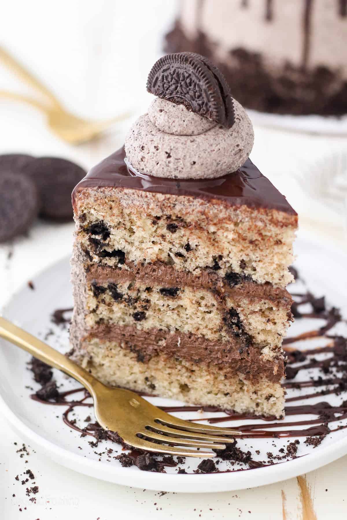 A slice of frosted Oreo cookies and cream cake on a plate next to a fork.