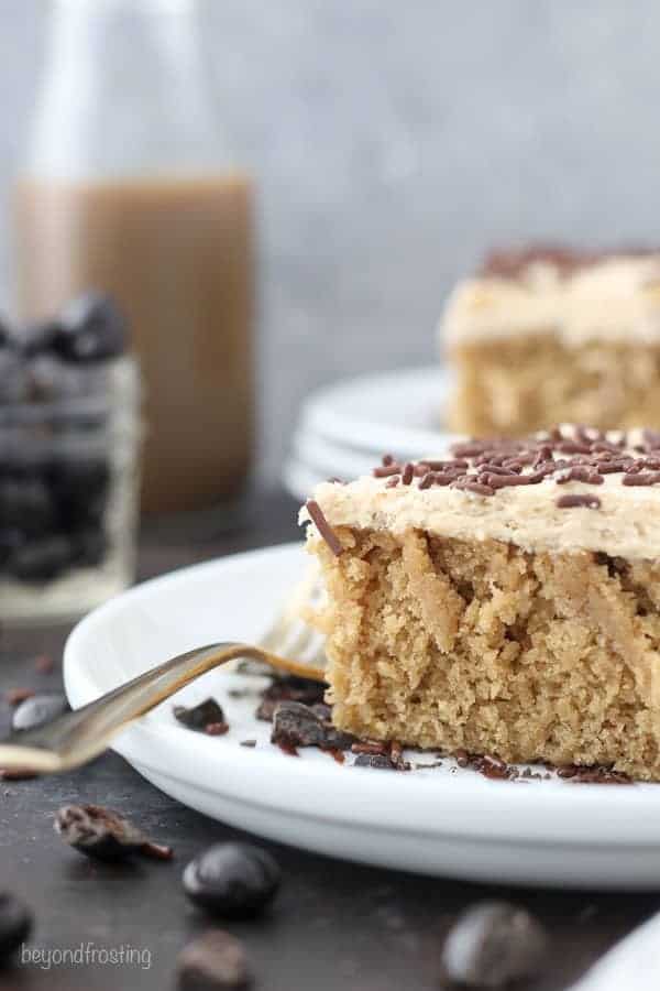  Vue de côté d'une tranche de gâteau moka humide sur une assiette à gâteau blanche avec une fourchette en or.