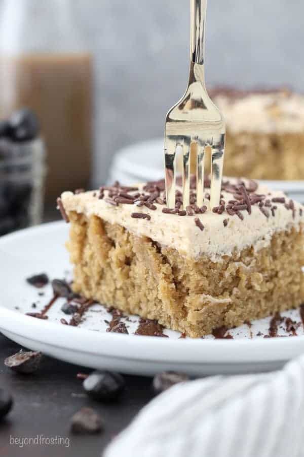  Une fourchette s'enfonçant dans une tranche de gâteau au moka sur une assiette blanche arrosée de chocolat et de grains d'espresso écrasés.