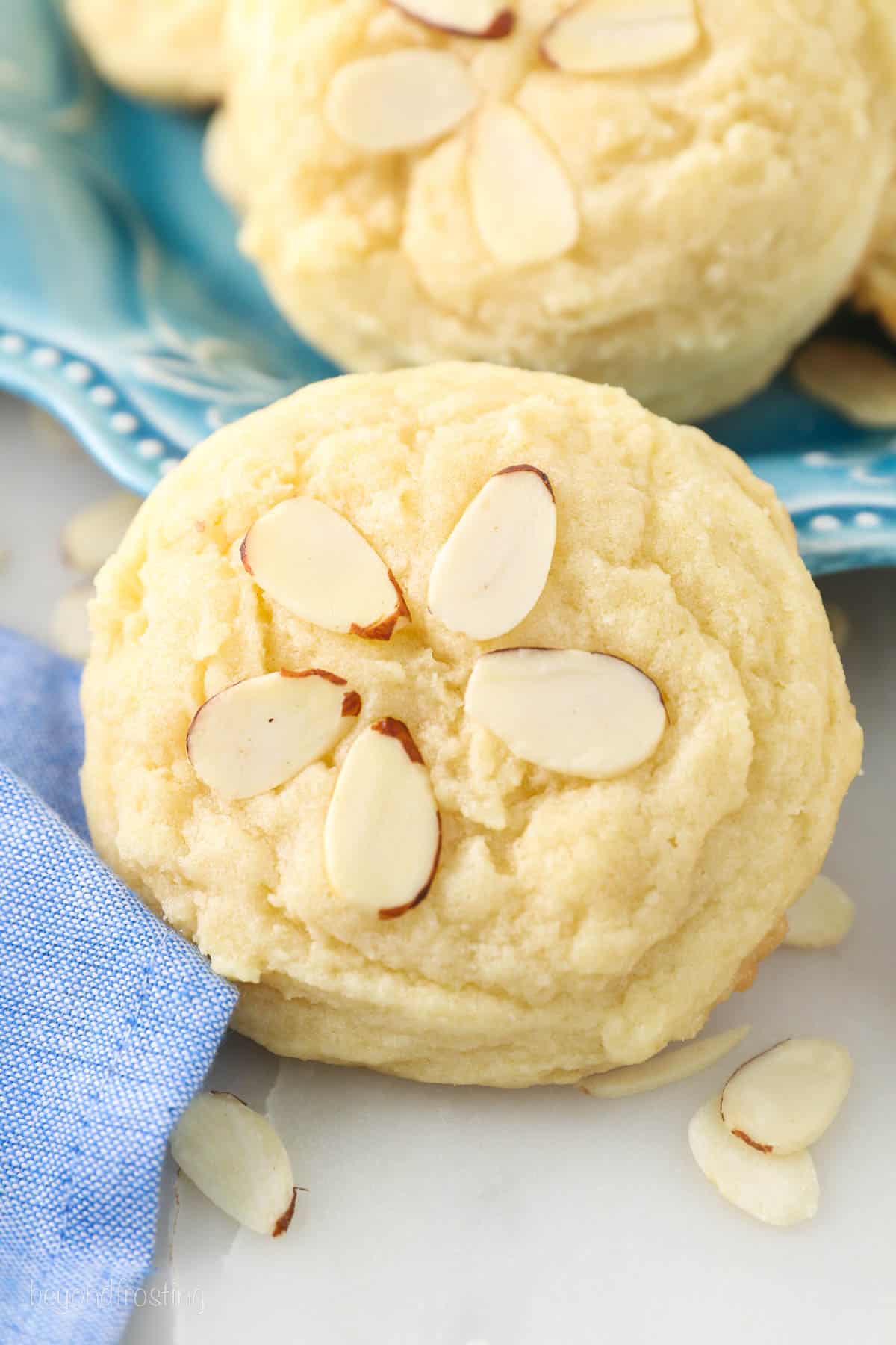 Close up of a almond cookie decorated with sliced almonds, with more cookies on a plate in the background.