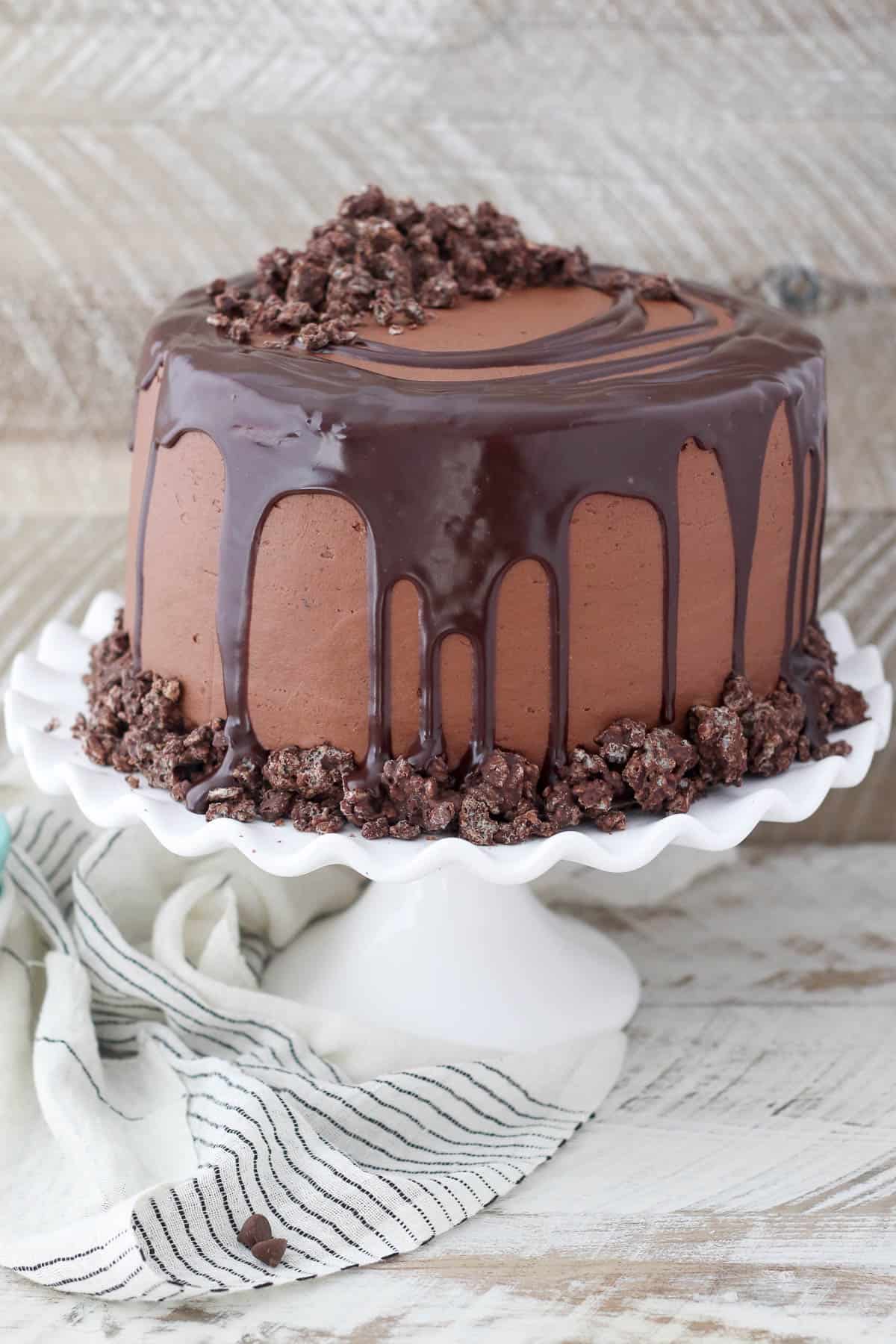A frosted French Silk chocolate cake topped with a ganache drip on a cake stand.