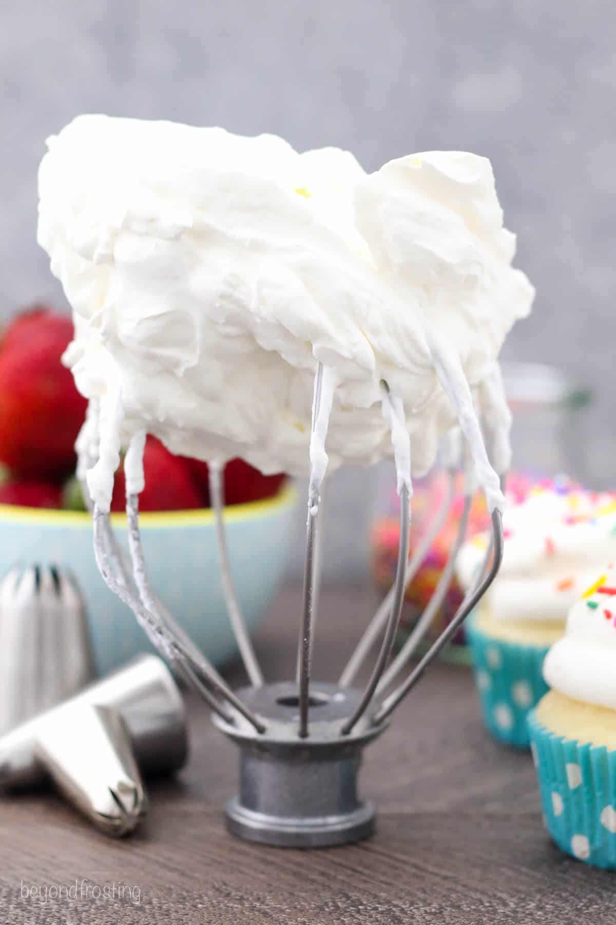 A wire whisk attachment standing upright, topped with stiff, fluffy whipped cream.