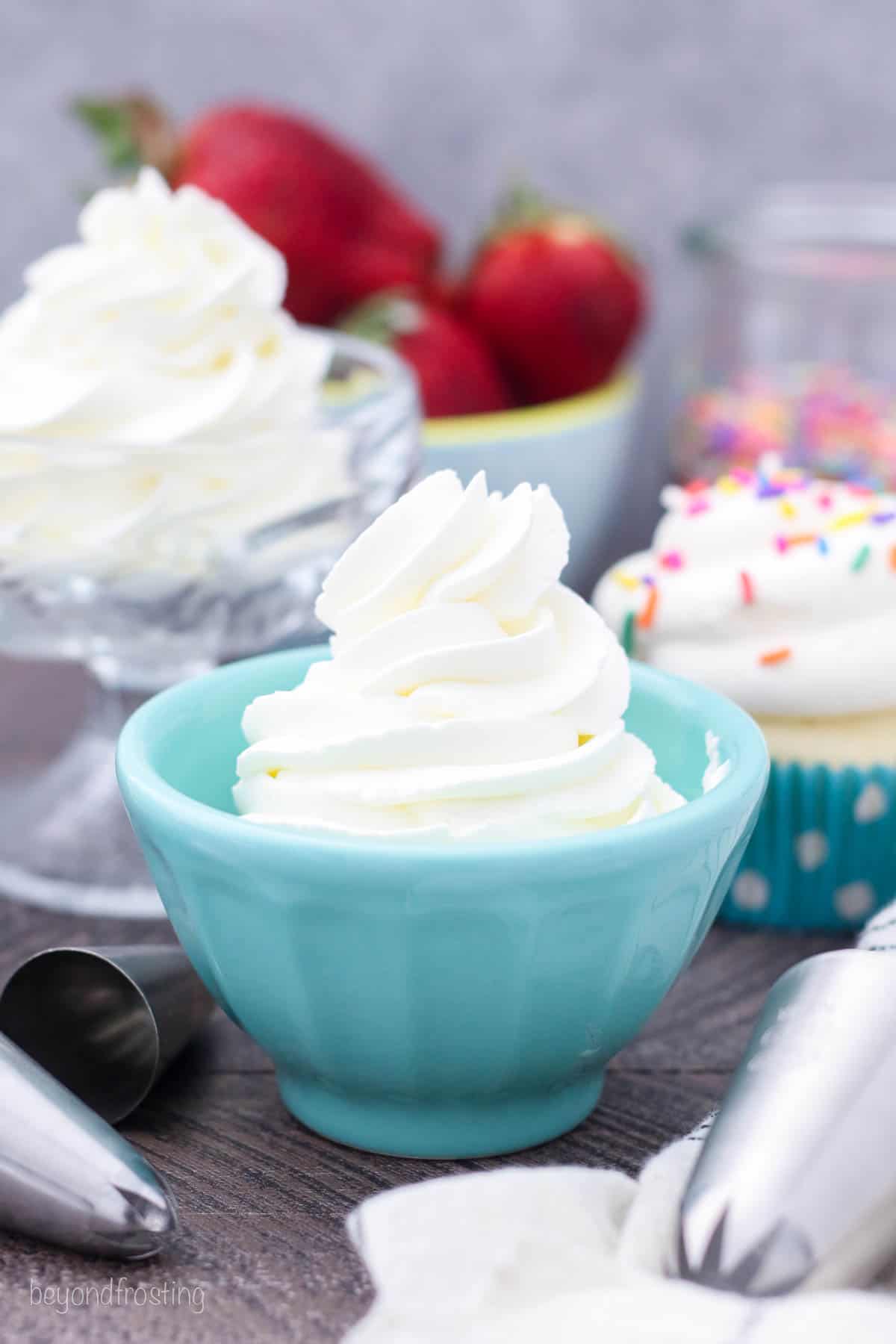 Whipped cream piped into a teal dish with more whipped cream and a bowl of strawberries in the background.