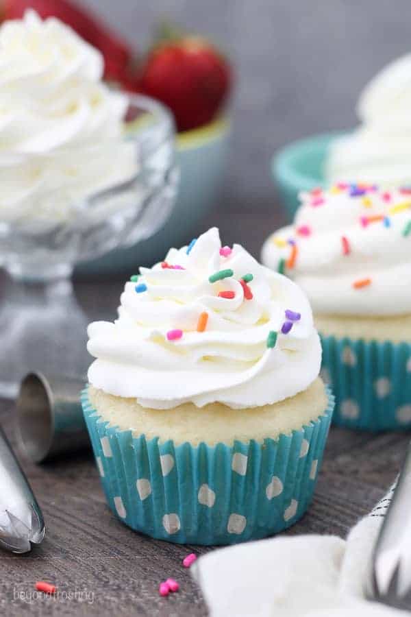 A cupcake topped with piped whipped cream frosting and sprinkles