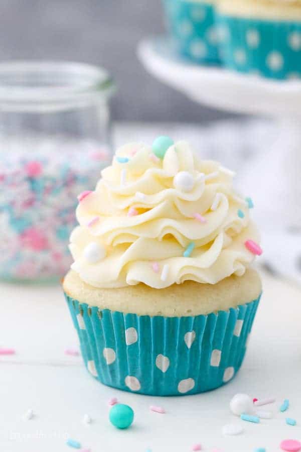 A single vanilla cupcake in a teal polka dot liner topped with beautifully pipped vanilla buttercream and sprinkles