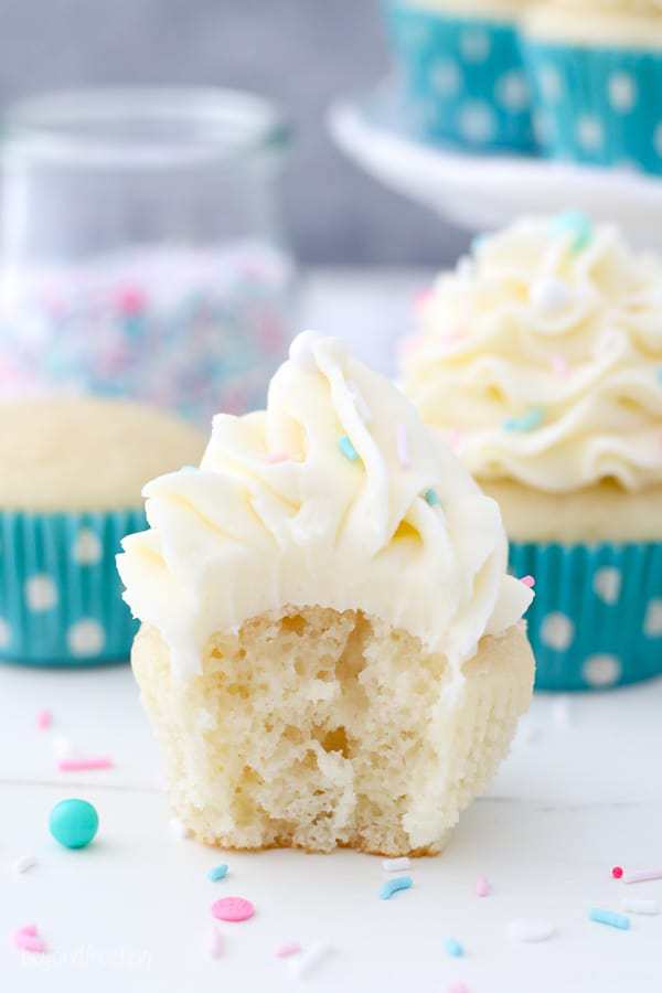 Ein feuchter Vanille-Cupcake mit Vanille-Glasur und Streuseln hat einen großen Biss