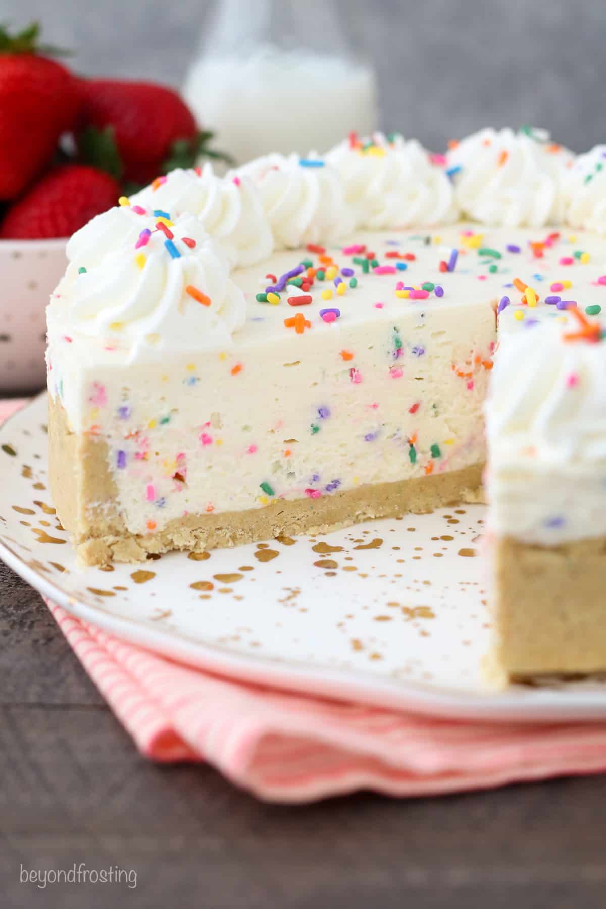 Funfetti cheesecake decorated with whipped cream and sprinkles with a slice missing.