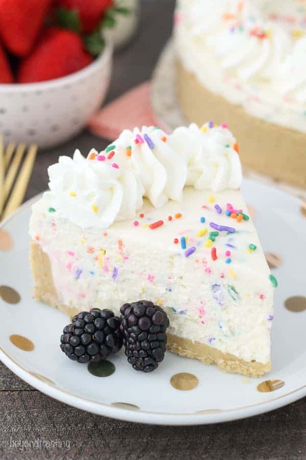 A overhead view of a No-Bake Funfetti Cheesecake on a gold polka dot plate with blackberries and sprinkles