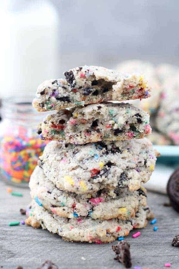 A tall stack of cookie, two of which are broken in half to show the middle which is stuffed with Oreos and sprinkles.