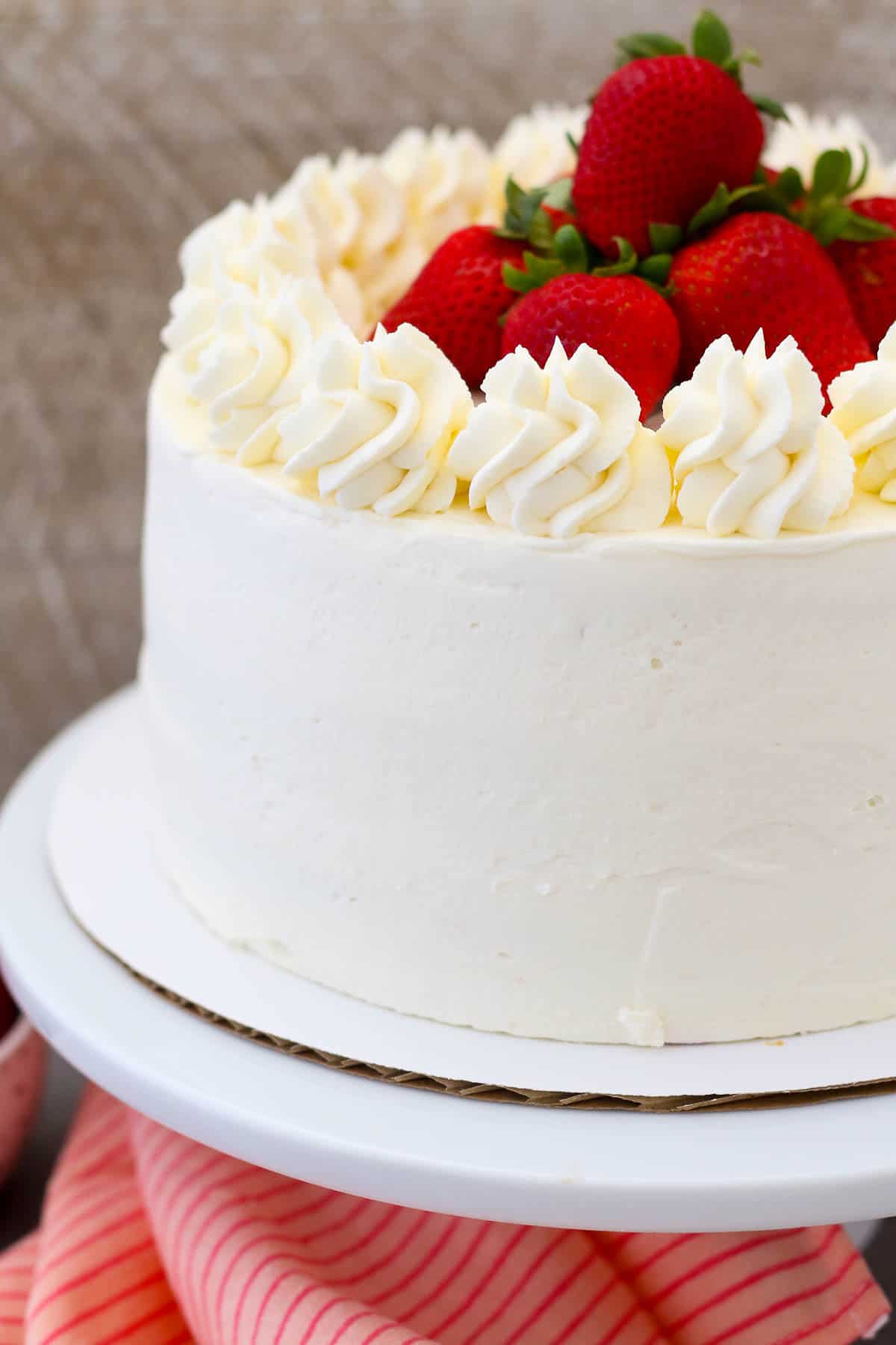 A frosted strawberry mascarpone cake topped with frosting swirls and fresh strawberries on a cake stand.