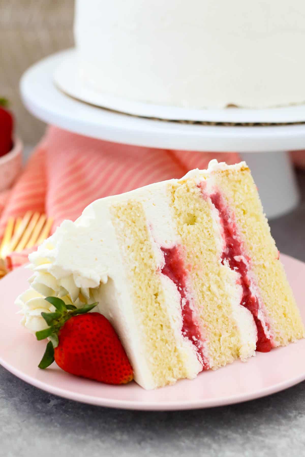 A slice of strawberry mascarpone cake on a pink plate garnished with a fresh strawberry.