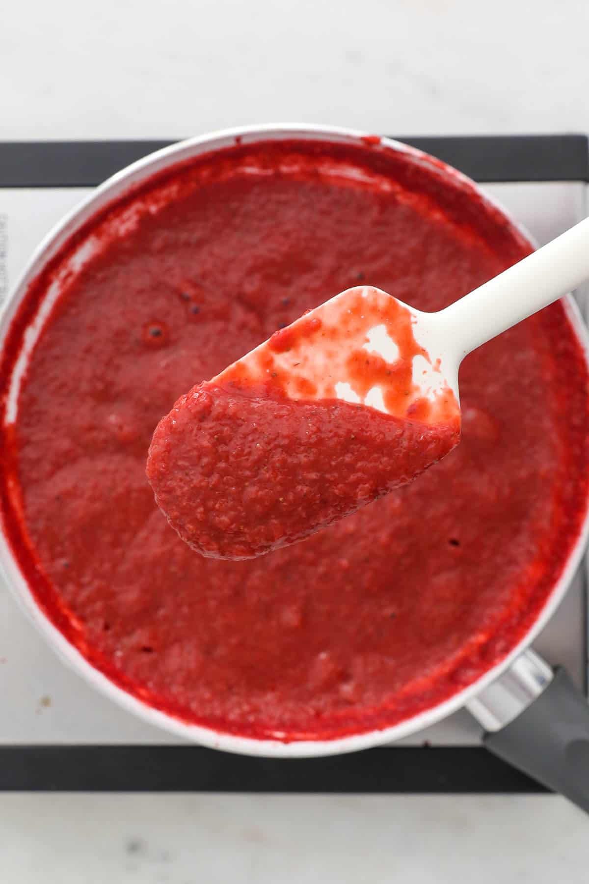 Overhead view of strawberry puree stirred with a spatula in a skillet.