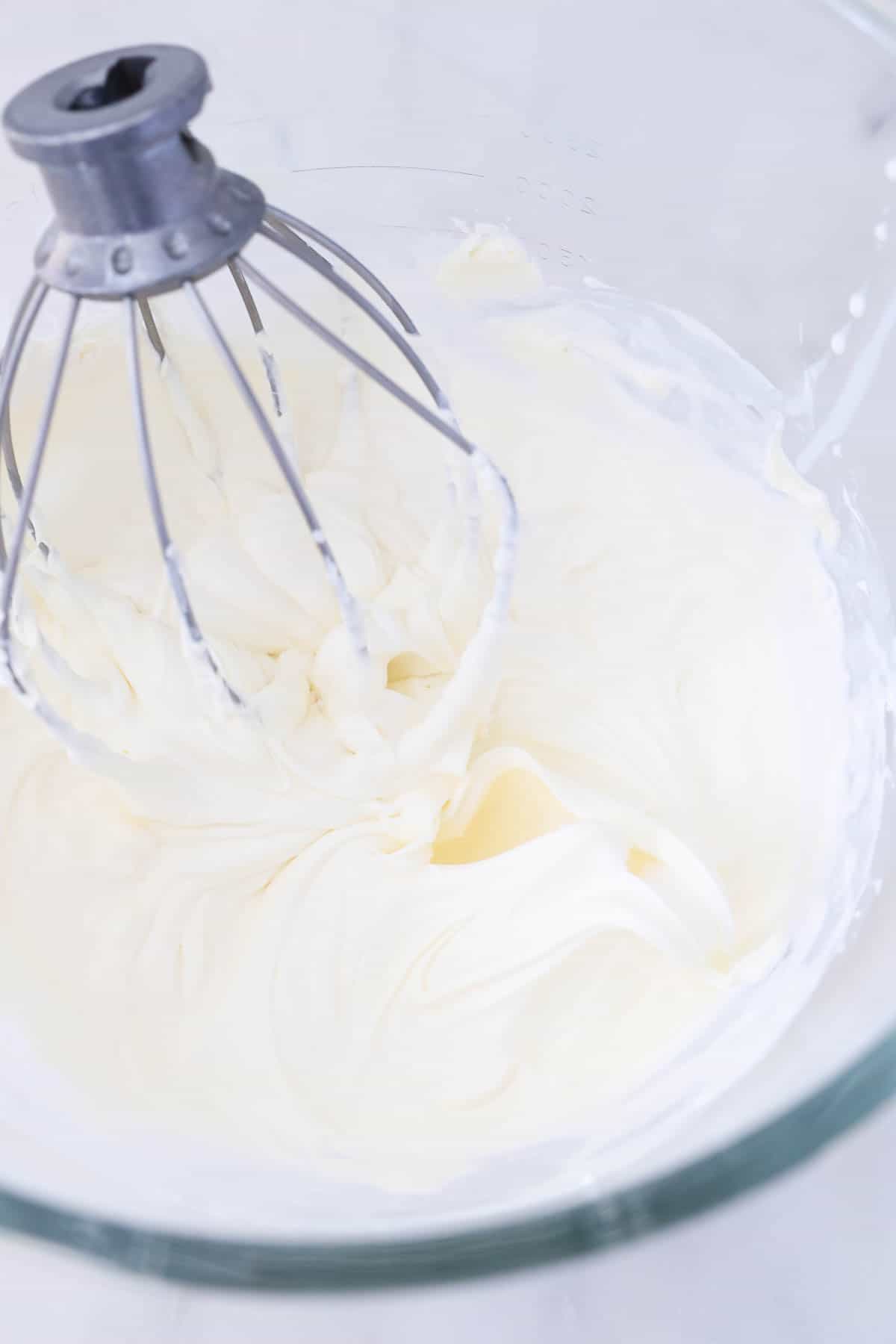 Mascarpone whipped cream inside a glass mixing bowl with a stand mixer whisk attachment.