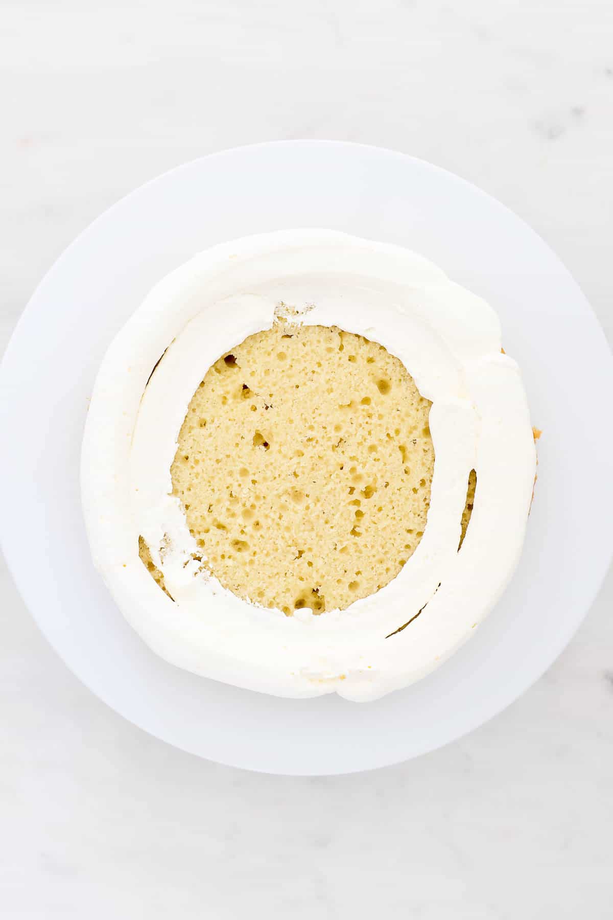 Overhead view of mascarpone whipped cream piped around the edge of a cake layer to form a "dam" for the strawberry filling.