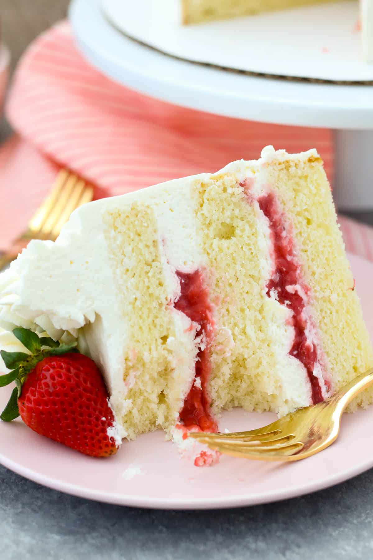 A slice of strawberry mascarpone cake on a pink plate garnished with a fresh strawberry, next to a fork.