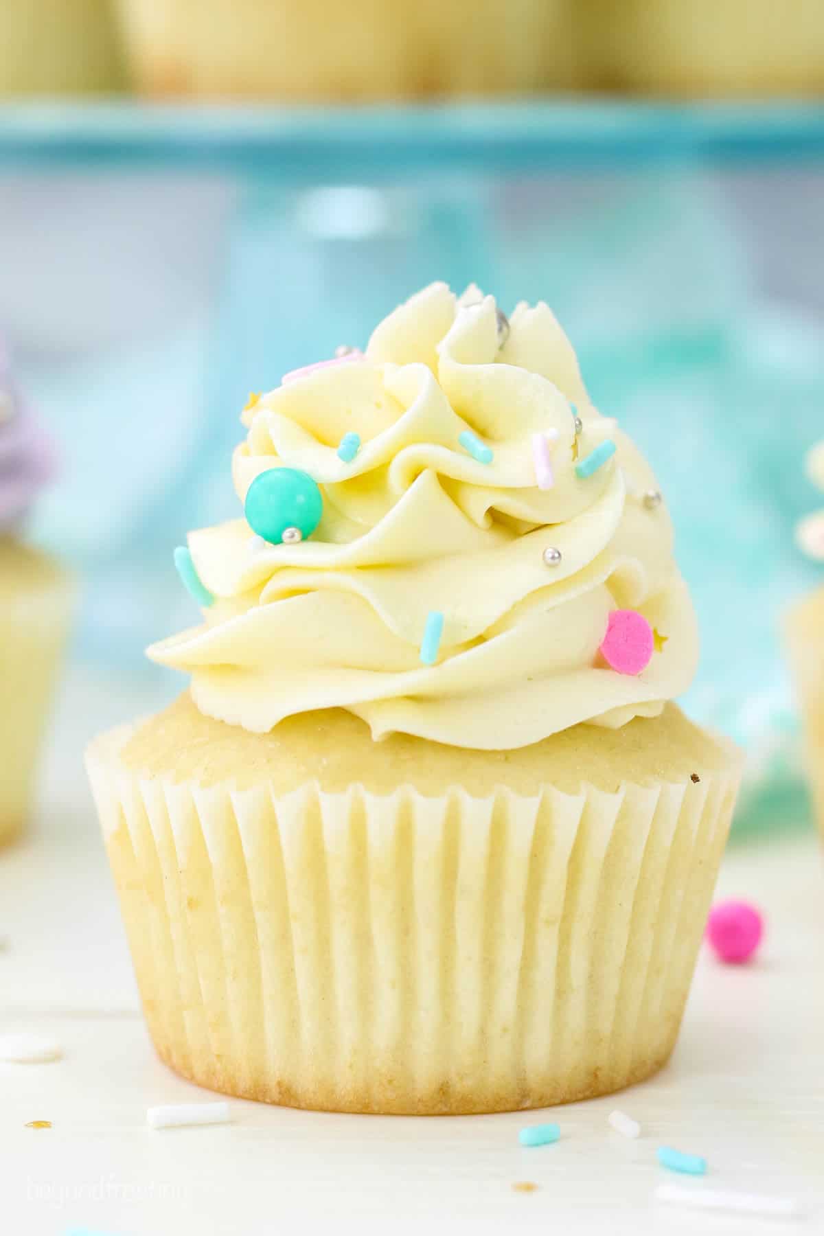 Close up of a vanilla cupcake frosted with a swirl of white Swiss meringue buttercream frosting.