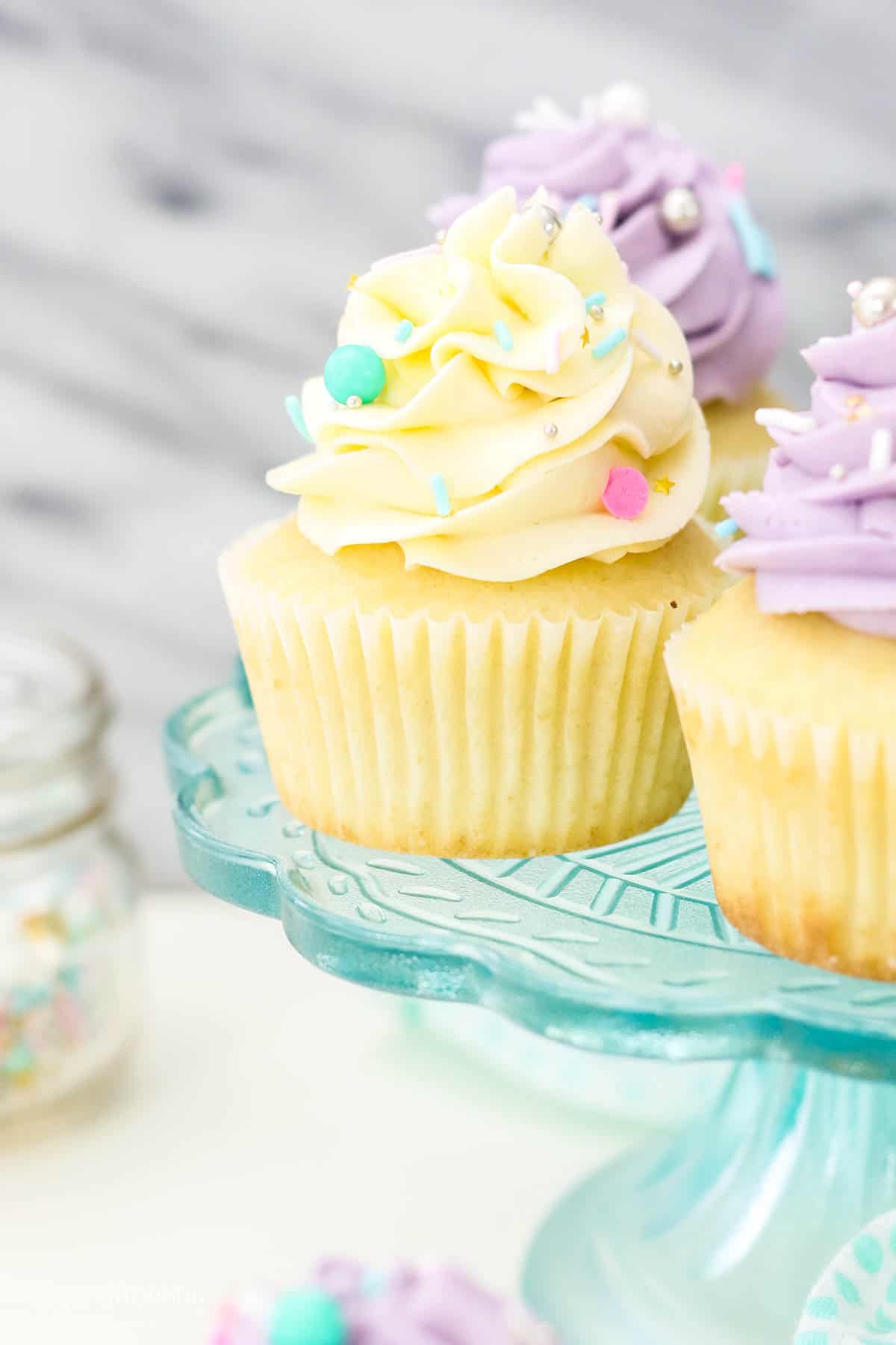 Assorted cupcakes on a cake stand frosted with swirls of Swiss meringue buttercream frosting.