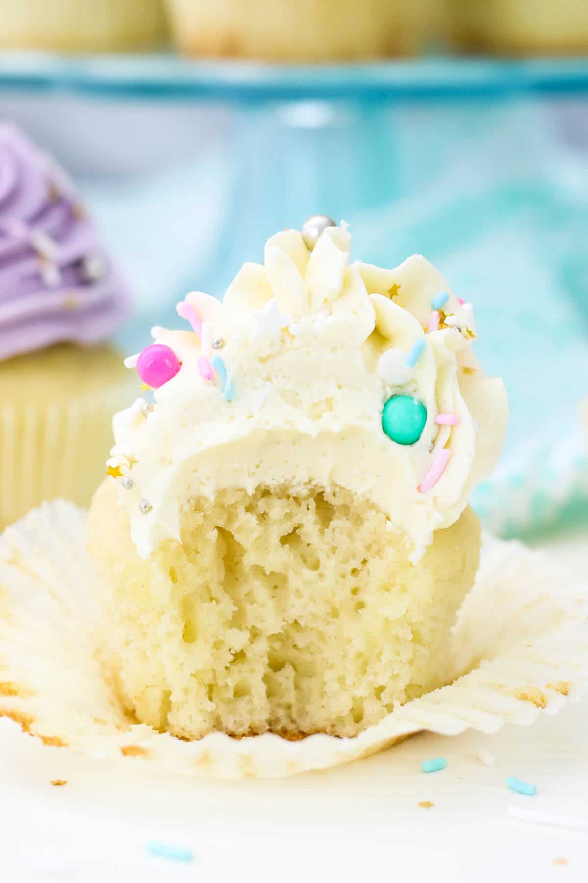 Close up of a vanilla cupcake frosted with a swirl of white Swiss meringue buttercream frosting with a bite missing.