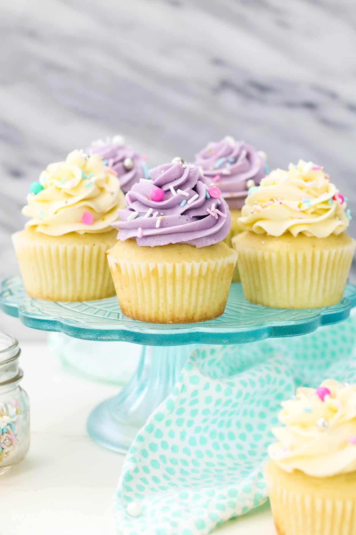 Assorted cupcakes on a cake stand frosted with swirls of Swiss meringue buttercream frosting.