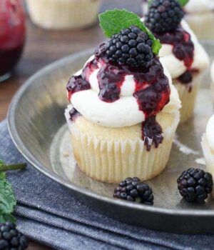 An overhead view of a cupcake covered with vanilla frosting and a blackberry sauce, The cupcake is garnished with a mint leaf