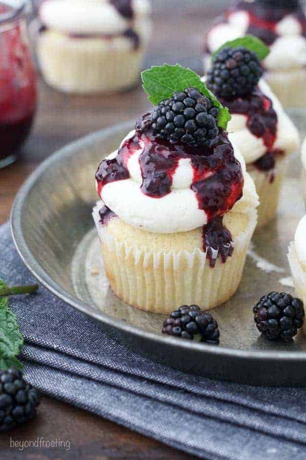 An overhead view of a cupcake covered with vanilla frosting and a blackberry sauce, The cupcake is garnished with a mint leaf