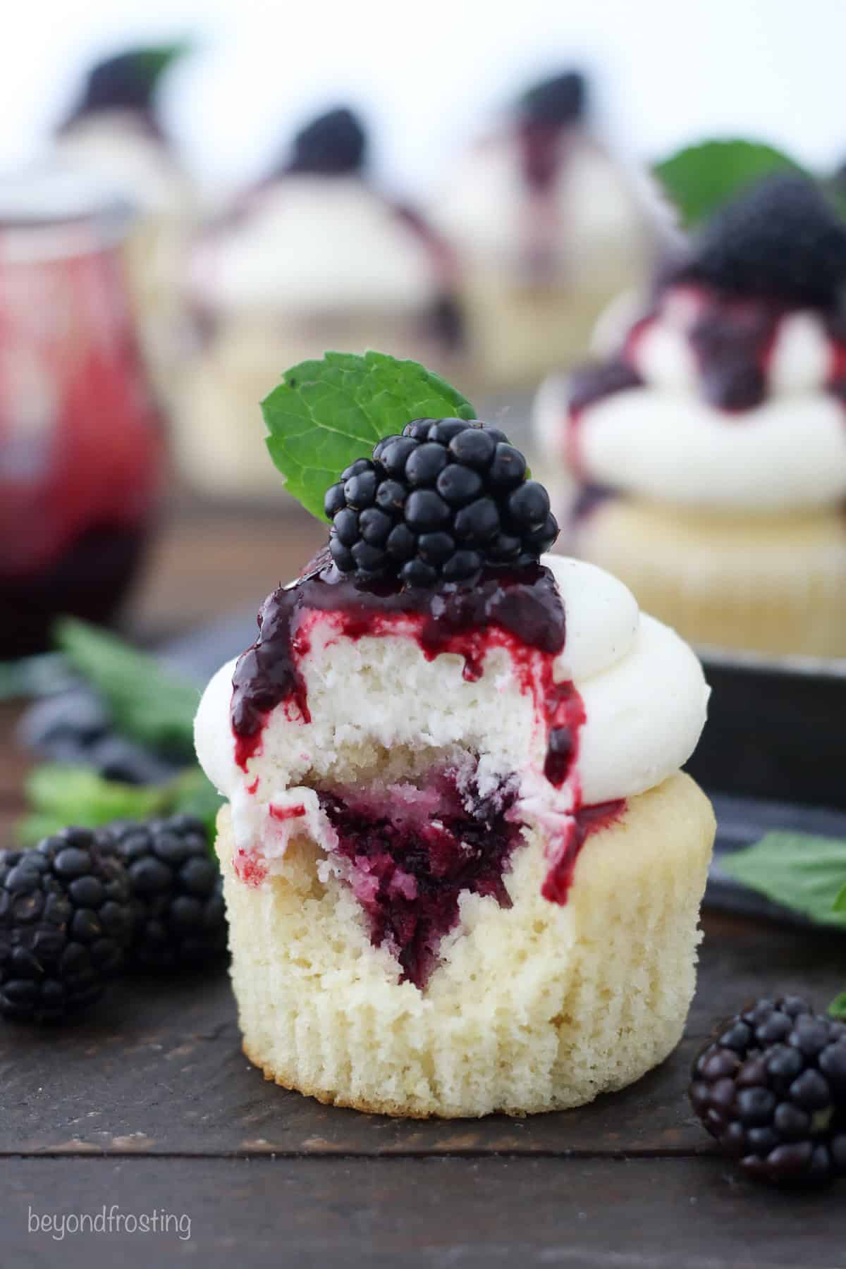 A bourbon smash cupcake with a bite missing, garnished with blackberry sauce, a fresh blackberry, and a mint leaf.