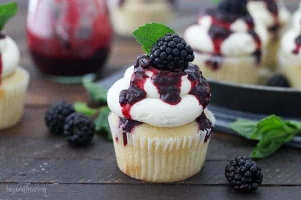 A bourbon infused vanilla cupcake covered with a vanilla buttercream and drizzled with blackberry sauce and a mint leaf garnish.