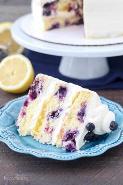 A slice of cake on a teal plate. the cake appears to be loaded with blueberries and a lemon curd.