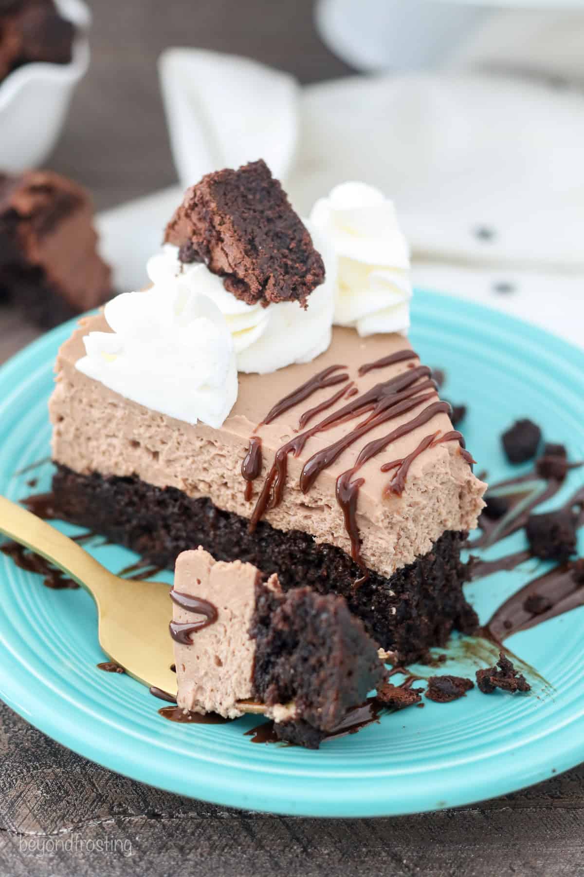 A forkful of brownie bottom cheesecake resting next to a cheesecake slice on a blue plate.