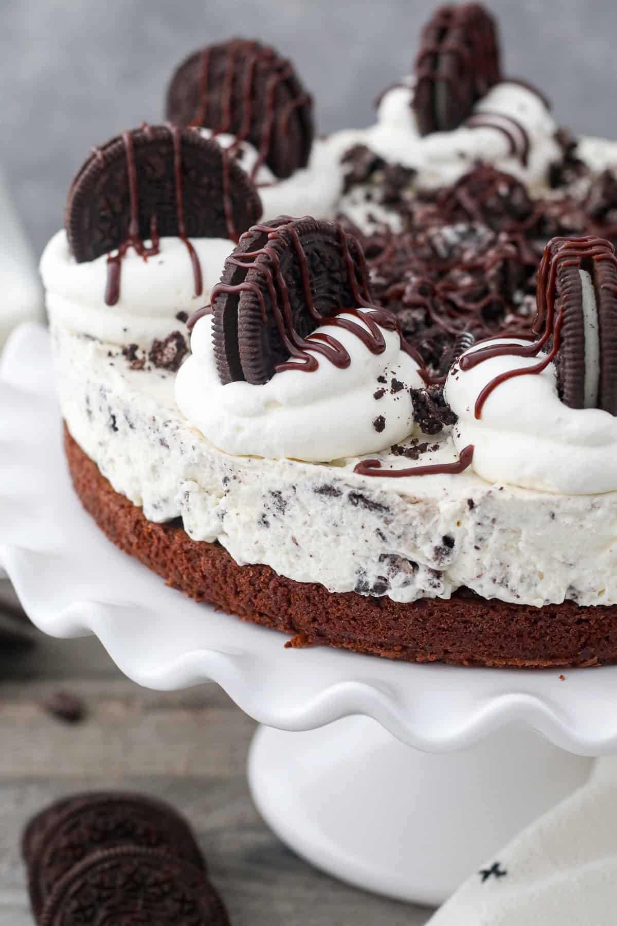 This Oreo mousse pie layers a fudgy brownie with silky white chocolate mousse and lots of crushed Oreos! It's a fun & easy make-ahead dessert. A whole Oreo mousse cake decorated with whipped cream, crushed Oreos, and chocolate sauce on a cake stand.