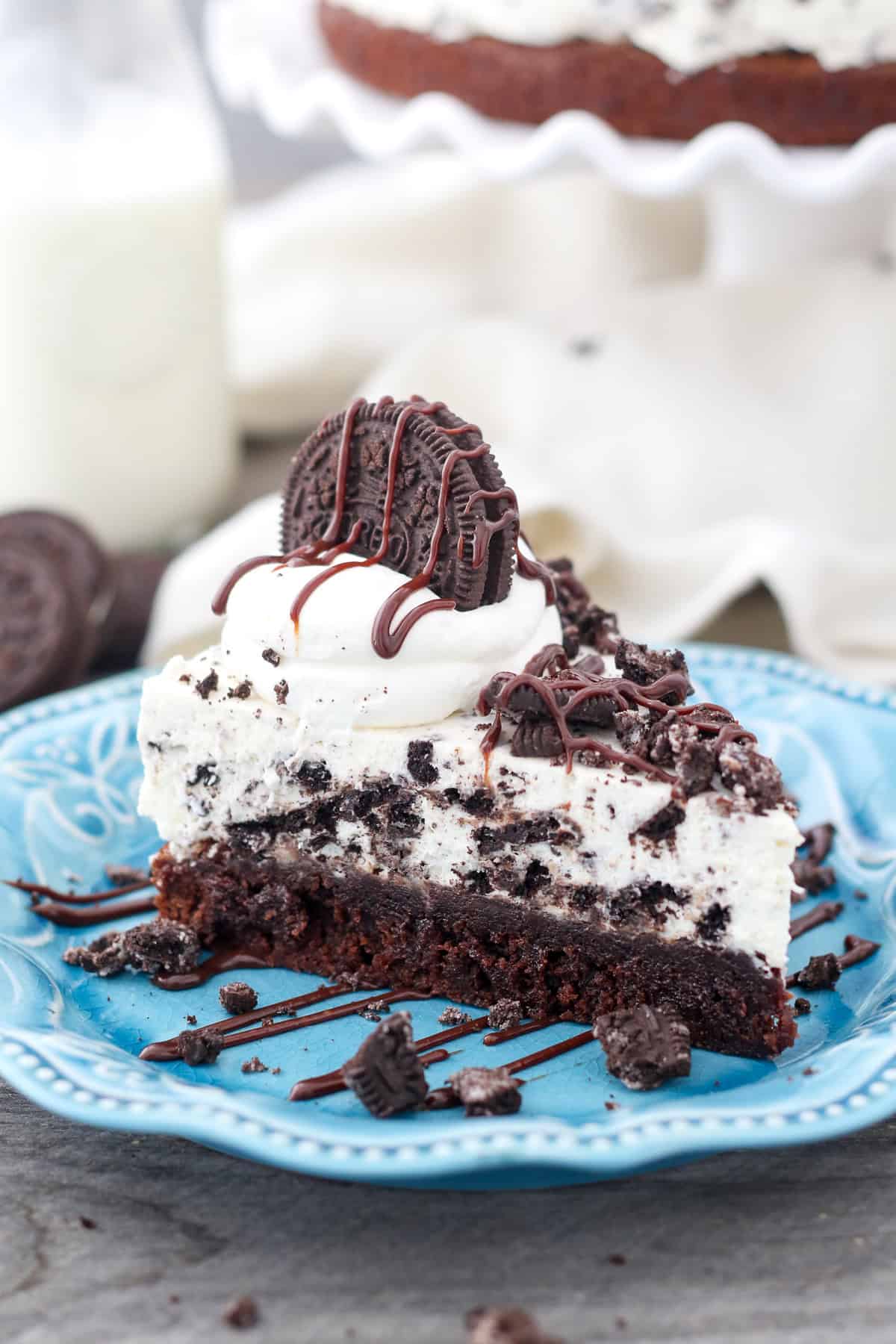 This Oreo mousse pie layers a fudgy brownie with silky white chocolate mousse and lots of crushed Oreos! It's a fun & easy make-ahead dessert. A slice of Oreo mousse cake topped with whipped cream, crushed Oreos, and chocolate cause on a plate.