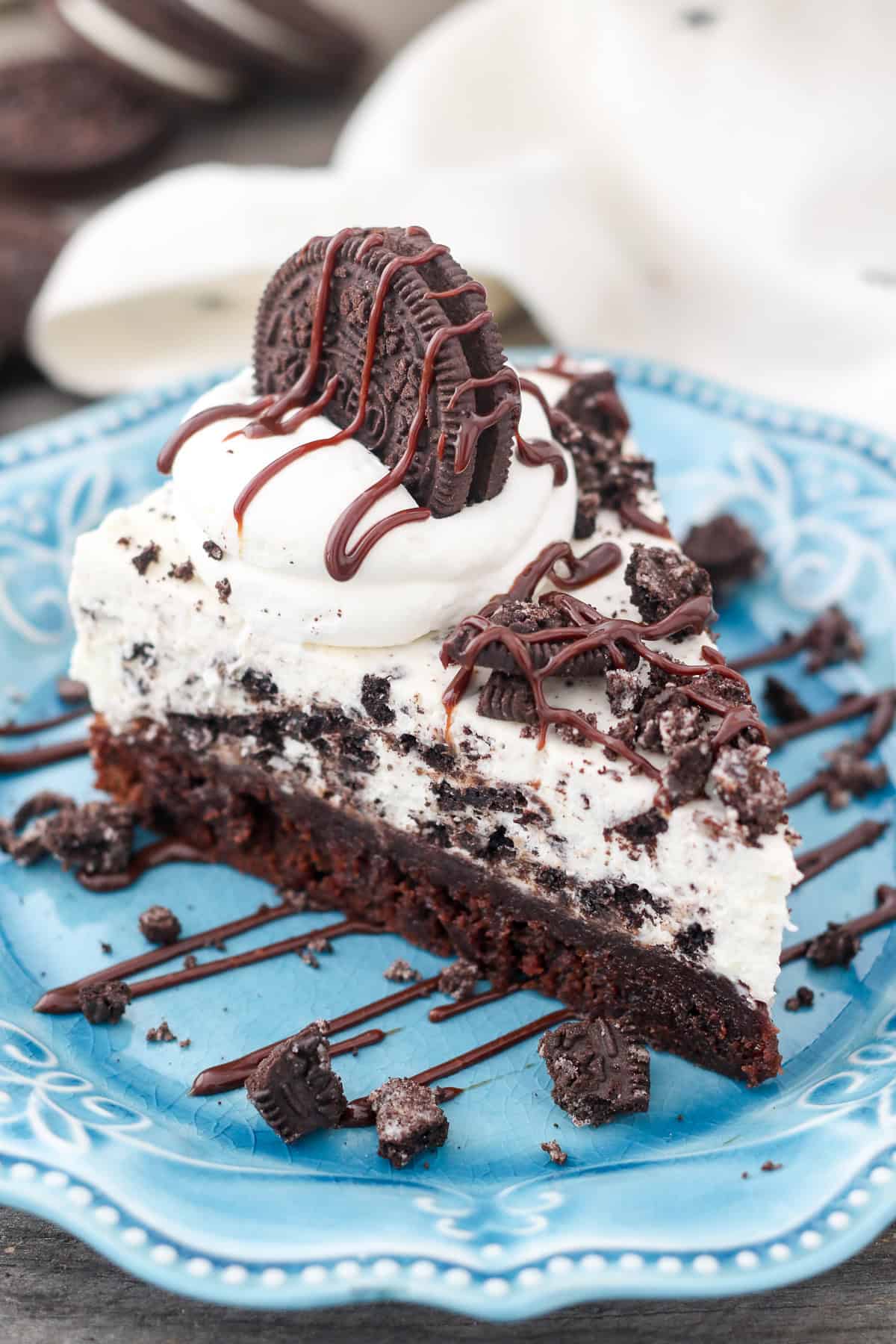 This Oreo mousse pie layers a fudgy brownie with silky white chocolate mousse and lots of crushed Oreos! It's a fun & easy make-ahead dessert. A slice of Oreo mousse cake topped with whipped cream, crushed Oreos, and chocolate cause on a plate.
