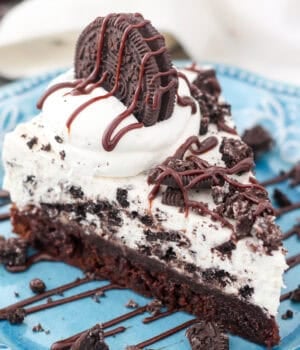 A slice of Oreo mousse cake topped with whipped cream, crushed Oreos, and chocolate cause on a plate.