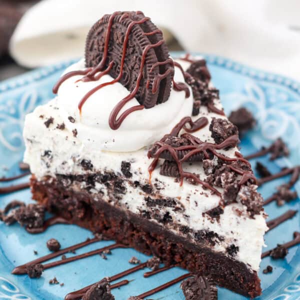 A slice of Oreo mousse cake topped with whipped cream, crushed Oreos, and chocolate cause on a plate.