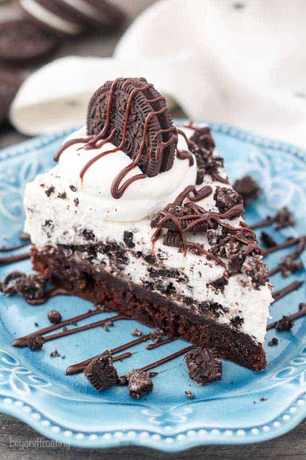 An overhead view of a slice of Oreo pie with a layer of brownie on the bottom. The top is garnished with more Oreos and hot fudge.