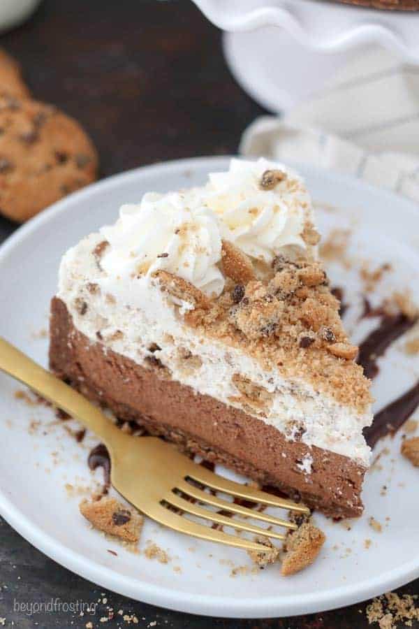 An overhead shot of a slice of chocolate chip cookie mousse cake on a white plate with a gold fork