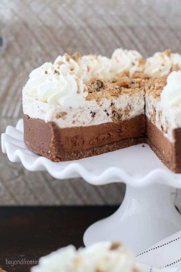 A shot of a Chocolate Chip Cookie Mousse cake with a slice taken out of it on a large white cake plate