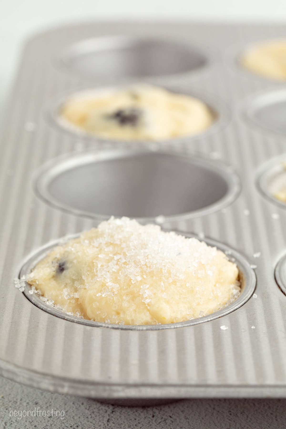 Close up of lemon blackberry muffin batter sprinkled with sanding sugar inside a muffin tin.