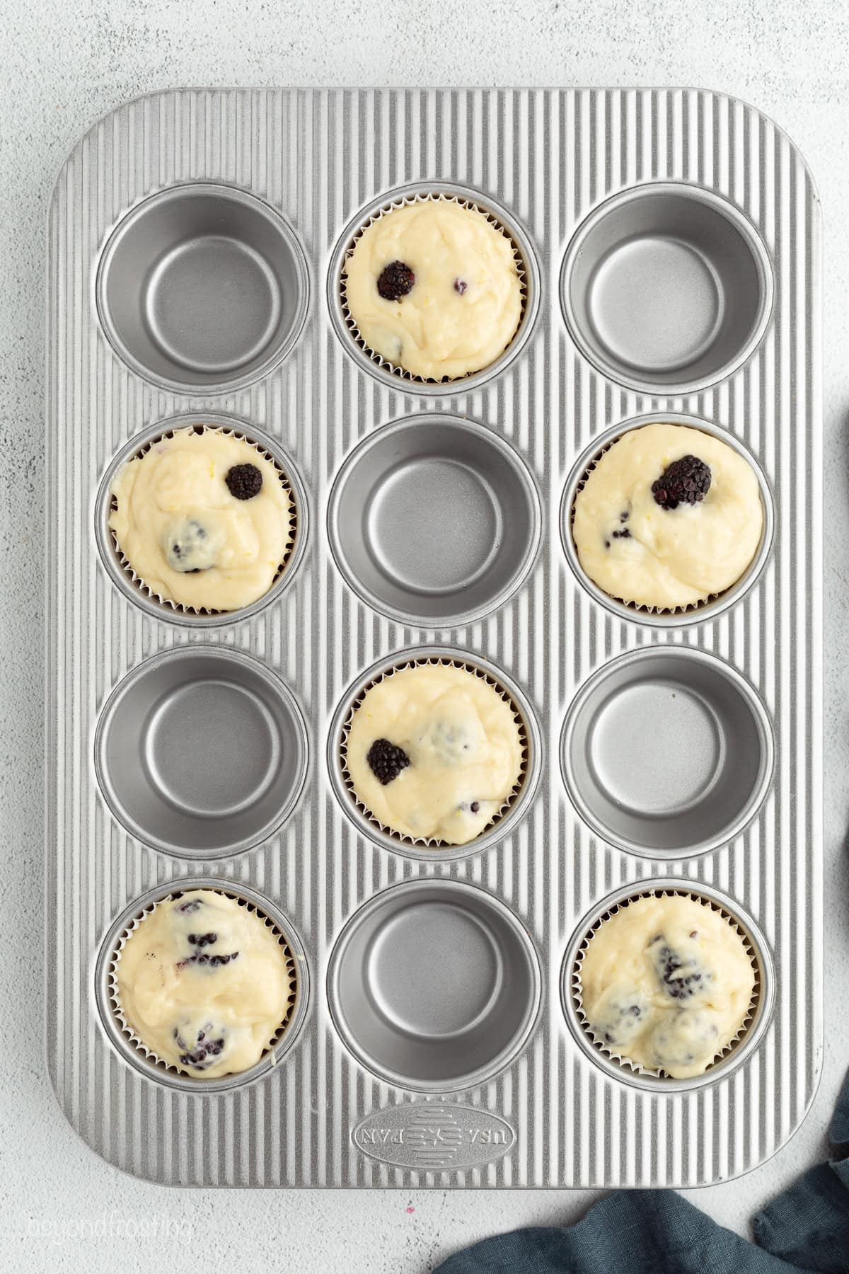 Overhead view of lemon blackberry muffin batter added to every other well in a muffin tin, with an empty well in between.