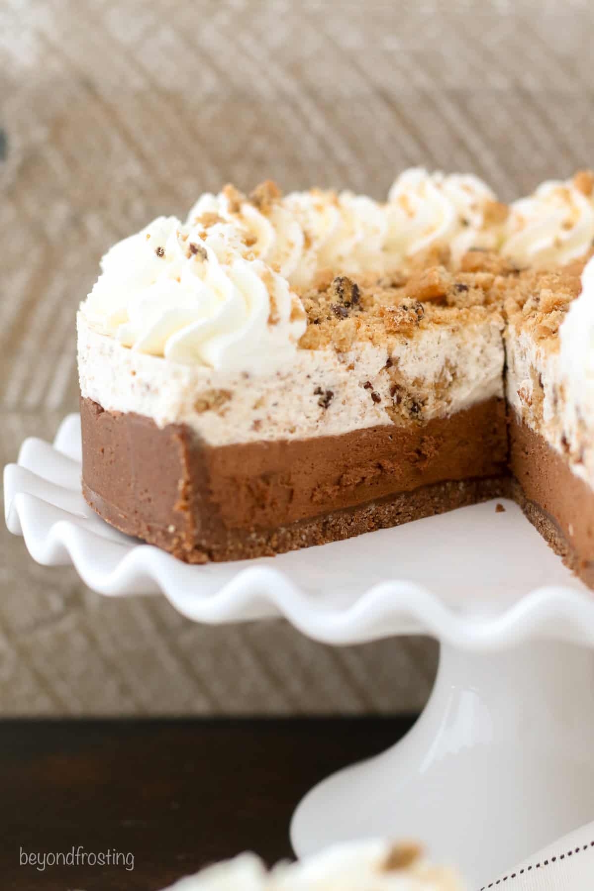 A no-bake chocolate chip cookie mousse cake with a large slice missing on a white cake stand.