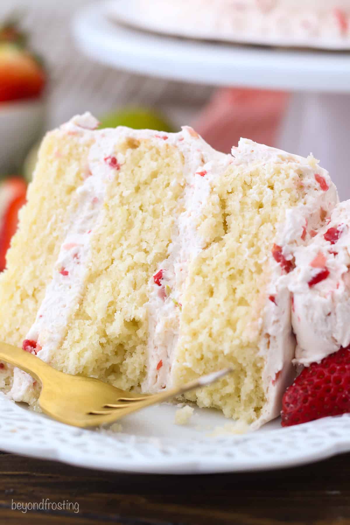 A slice of strawberry margarita layer cake on a plate next to a fork, with a bite missing.