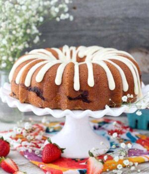 A large strawberry bundt cake on a white cake plate with a scallop edge