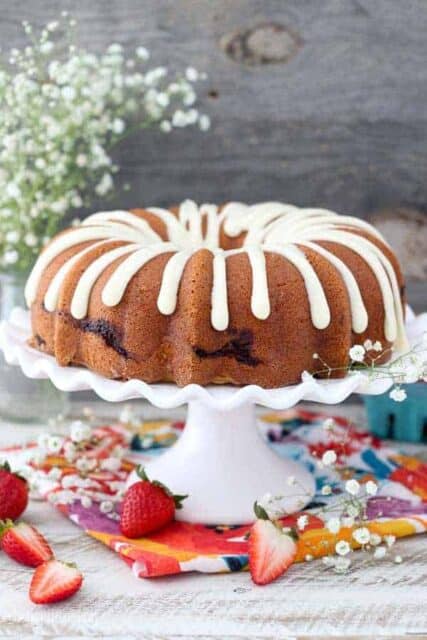 A large strawberry bundt cake on a white cake plate with a scallop edge